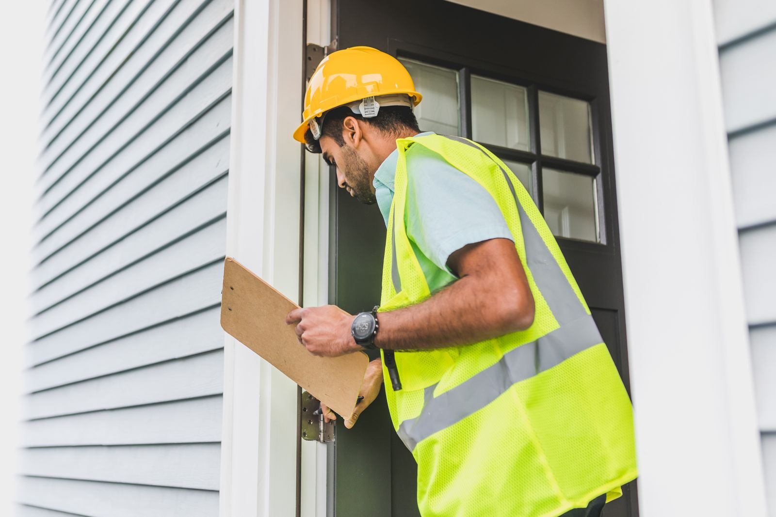 Inspector with clipboard and hard hat examining a house